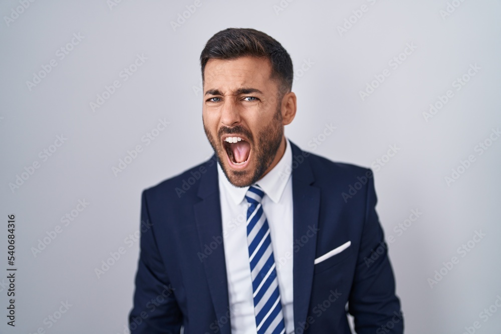 Handsome hispanic man wearing suit and tie angry and mad screaming frustrated and furious, shouting with anger. rage and aggressive concept. Handsome hispanic man wearing suit and tie angry and mad screaming frustrated and furious, shouting with anger. rage and aggressive concept.