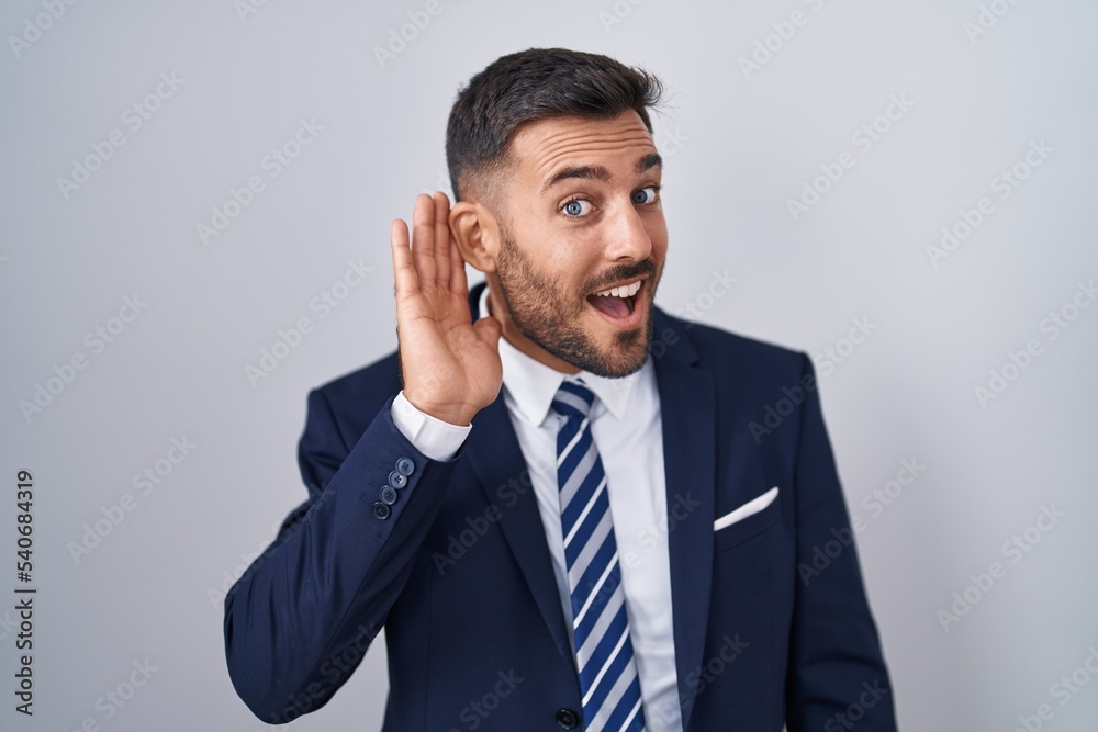 Handsome hispanic man wearing suit and tie smiling with hand over ear listening an hearing to rumor or gossip. deafness concept. Handsome hispanic man wearing suit and tie smiling with hand over ear listening an hearing to rumor or gossip. deafness concept.