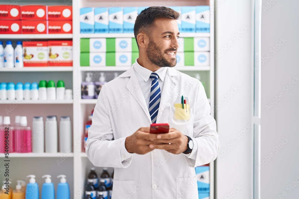 Young hispanic man pharmacist using smartphone working at pharmacy Young hispanic man pharmacist using smartphone working at pharmacy