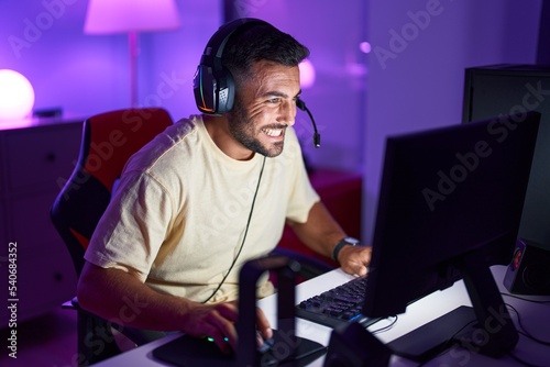 Young hispanic man streamer playing video game using computer at gaming room