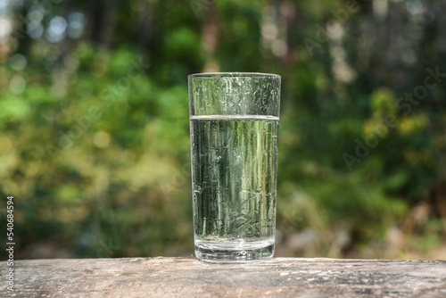 Glass of cool water on wooden surface outdoors
