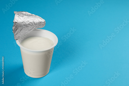 Plastic cup with tasty yogurt on light blue background, space for text
