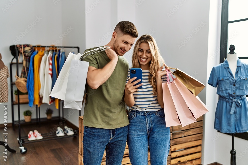 Young hispanic customer couple holding shopping bags and using smartphone at clothing store. Young hispanic customer couple holding shopping bags and using smartphone at clothing store.