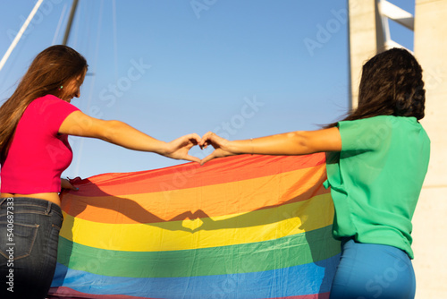 Happy couple of lesbian ladies making a heart sign with their hands.