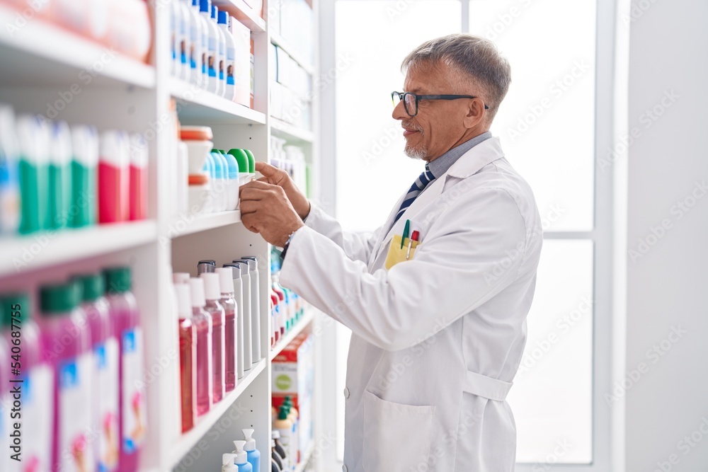 Middle age grey-haired man pharmacist holding deodorant bottle at laboratory Middle age grey-haired man pharmacist holding deodorant bottle at laboratory