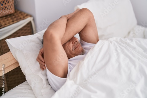 Middle age grey-haired man stressed lying on bed at bedroom