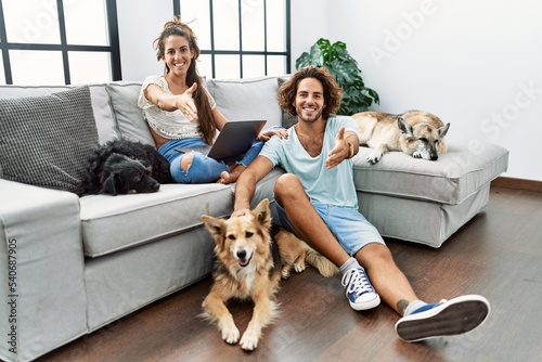 Sticker Young hispanic couple with dogs relaxing at home smiling friendly offering handshake as greeting and welcoming