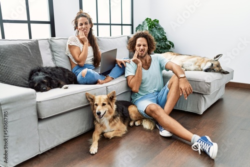 Young hispanic couple with dogs relaxing at home touching mouth with hand with painful expression because of toothache or dental illness on teeth. dentist concept. © Krakenimages.com