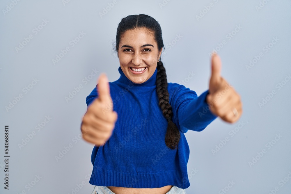 Young hispanic woman standing over isolated background approving doing positive gesture with hand, thumbs up smiling and happy for success. winner gesture. Young hispanic woman standing over isolated background approving doing positive gesture with hand, thumbs up smiling and happy for success. winner gesture.