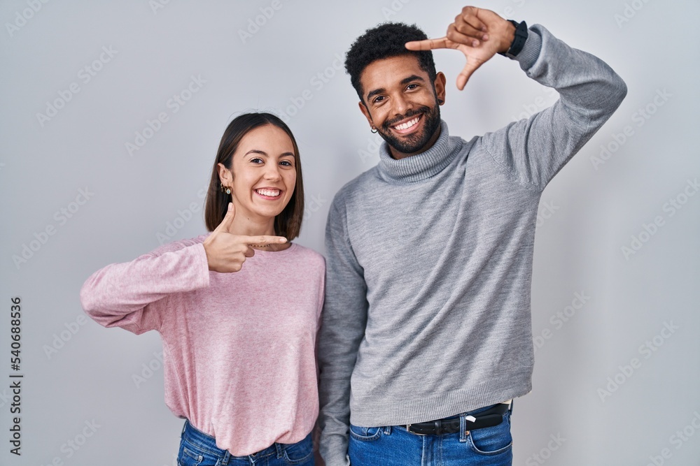 Fototapeta premium Young hispanic couple standing together smiling making frame with hands and fingers with happy face. creativity and photography concept.