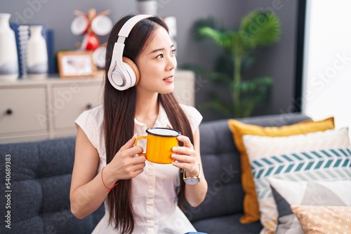 Young chinese woman listening to music drinking coffee at home
