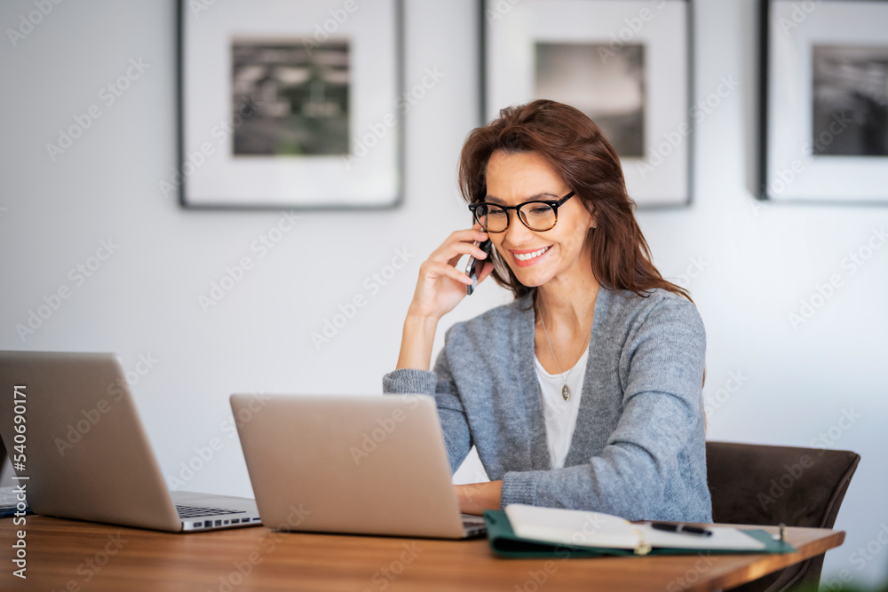 Business woman using mobile phone in front of laptops while working from home Business woman using mobile phone in front of laptops while working from home