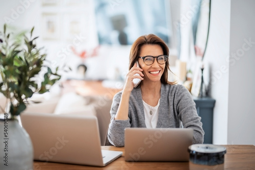Business woman using mobile phone in front of laptops while working from home