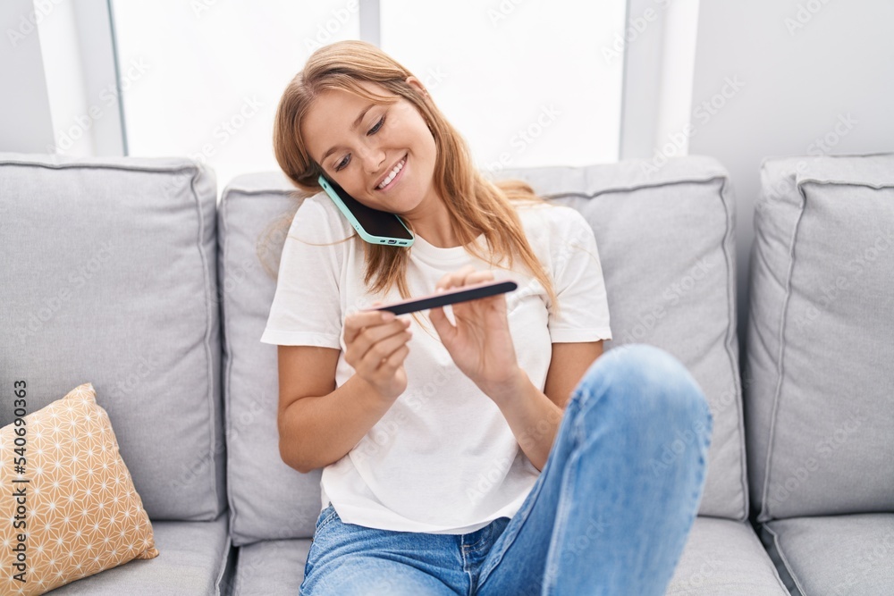 Young blonde girl talking on smartphone doing manicure at home Young blonde girl talking on smartphone doing manicure at home