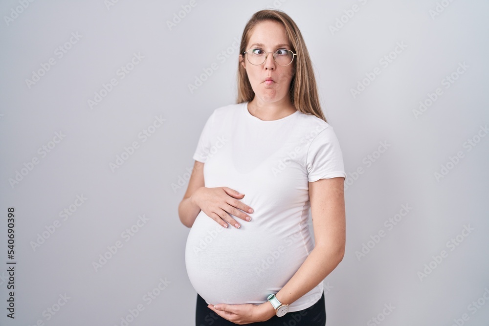 Young pregnant woman expecting a baby, touching pregnant belly making fish face with mouth and squinting eyes, crazy and comical.