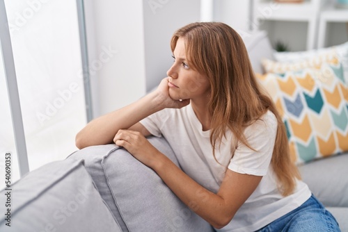 Young blonde girl sitting on sofa with serious expression at home