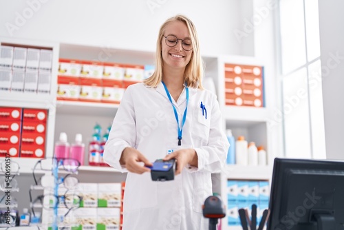 Young blonde woman pharmacist using credit card and dataphone at pharmacy
