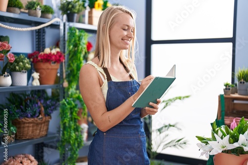 Young blonde woman florist smiling confident writing on book at florist store