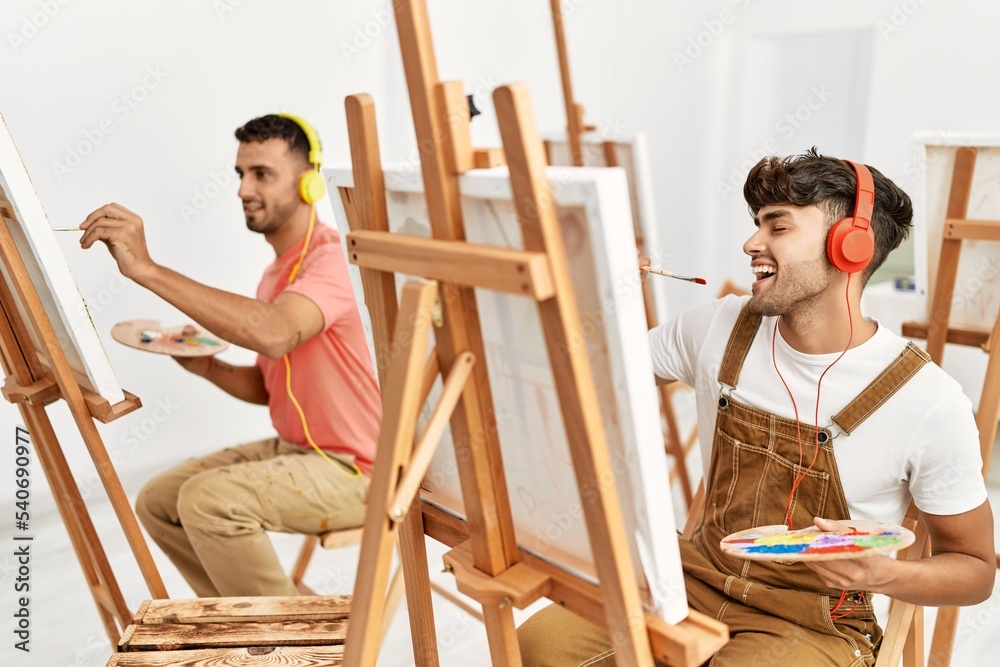 Two hispanic men couple listening to music and drawing at art studio
