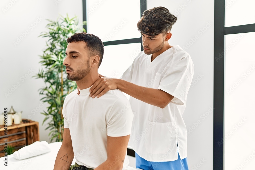 Fototapeta premium Two hispanic men physiotherapist and patient having rehab session massaging neck at clinic
