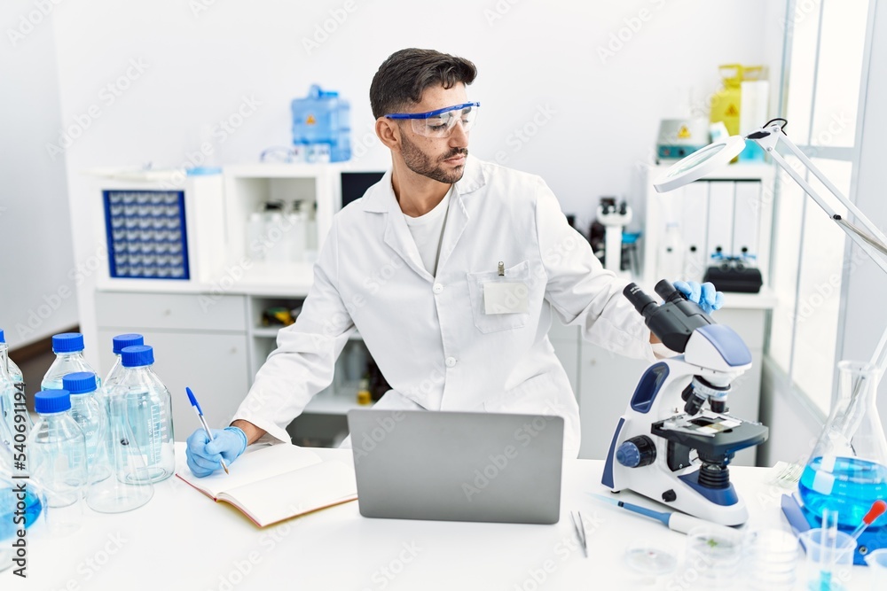 Handsome hispanic man working as scientific with microscope and laptop at laboratory Handsome hispanic man working as scientific with microscope and laptop at laboratory