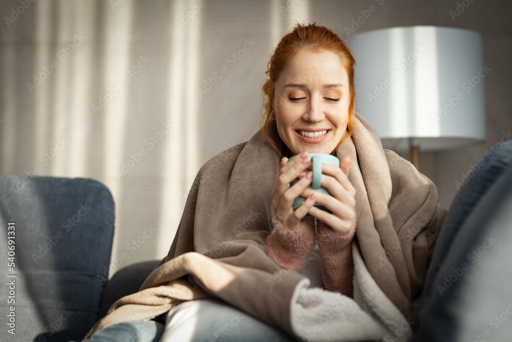 Woman with blanket over shoulders, siting on bed by the window in casual clothes enjoying her morning coffee Woman with blanket over shoulders, siting on bed by the window in casual clothes enjoying her morning coffee