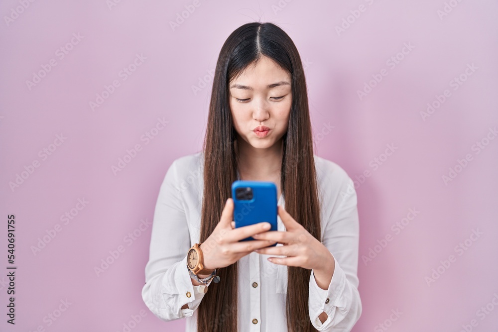 Chinese young woman using smartphone typing message puffing cheeks with funny face. mouth inflated with air, catching air. Chinese young woman using smartphone typing message puffing cheeks with funny face. mouth inflated with air, catching air.
