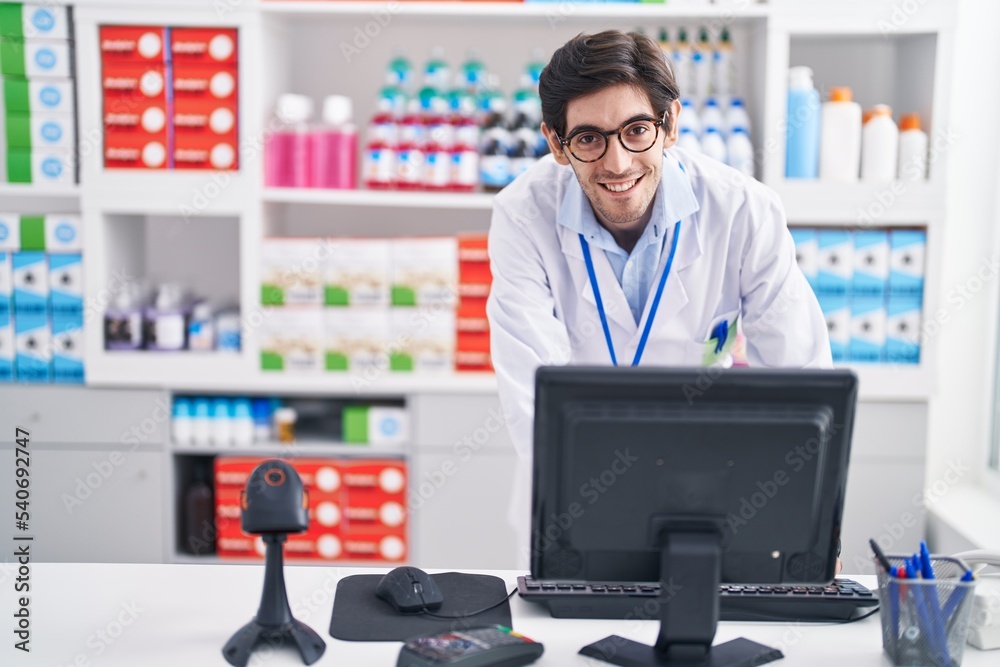 Young hispanic man pharmacist smiling confident using computer at pharmacy