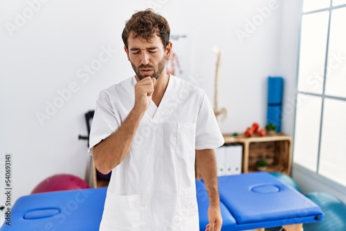 Young handsome physiotherapist man working at pain recovery clinic feeling unwell and coughing as symptom for cold or bronchitis. health care concept.