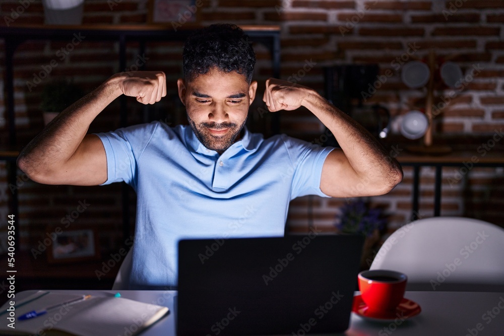 Hispanic man with beard using laptop at night showing arms muscles smiling proud. fitness concept. Hispanic man with beard using laptop at night showing arms muscles smiling proud. fitness concept.