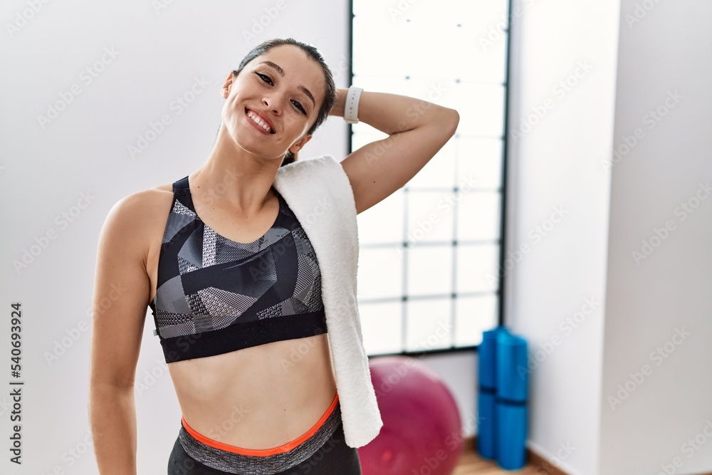 Young brunette woman wearing sportswear and towel at the gym smiling confident touching hair with hand up gesture, posing attractive and fashionable