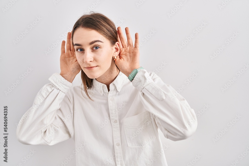 Young caucasian woman standing over isolated background trying to hear both hands on ear gesture, curious for gossip. hearing problem, deaf Young caucasian woman standing over isolated background trying to hear both hands on ear gesture, curious for gossip. hearing problem, deaf