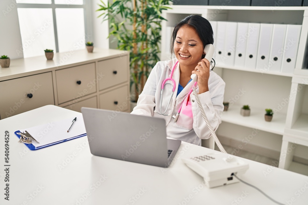 Young chinese woman wearing doctor uniform talking on the telephone at clinic