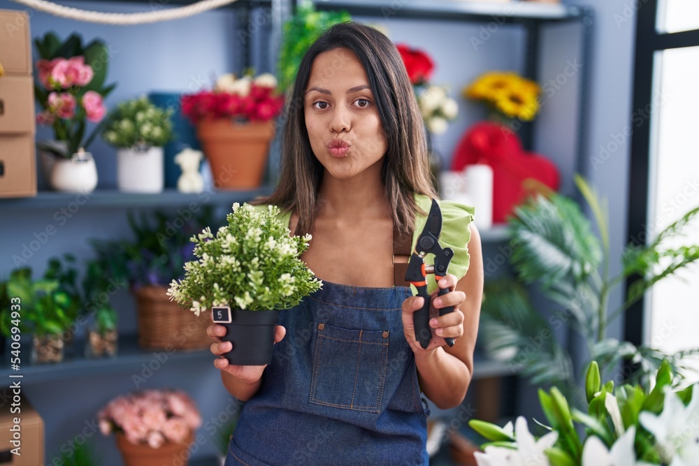 Hispanic young woman working at florist shop looking at the camera blowing a kiss being lovely and sexy. love expression.