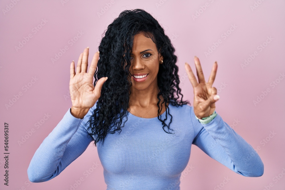 Middle age hispanic woman standing over pink background showing and pointing up with fingers number eight while smiling confident and happy.