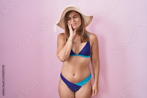 Young hispanic woman wearing bikini over pink background touching mouth with hand with painful expression because of toothache or dental illness on teeth. dentist
