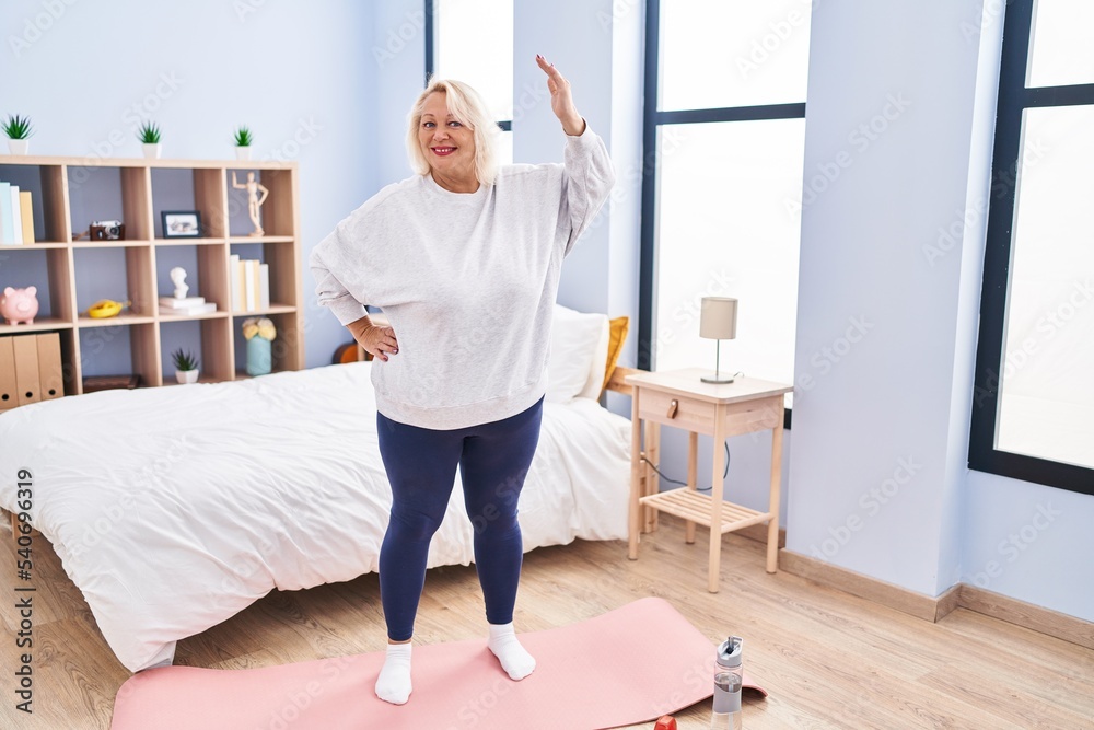 Middle age blonde woman smiling confident stretching at bedroom