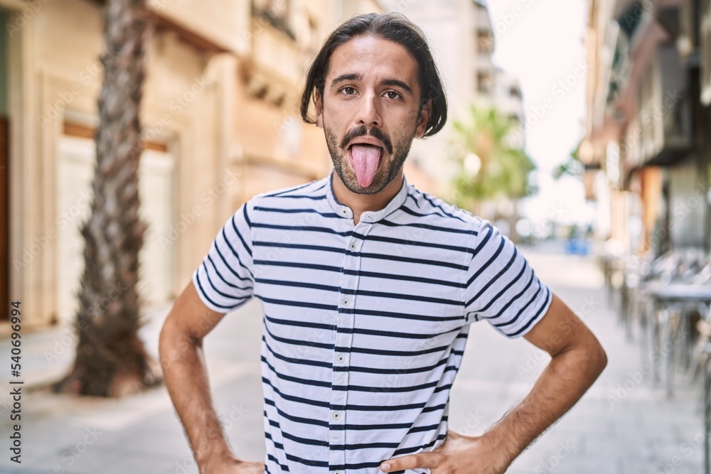 Young hispanic man with beard outdoors at the city sticking tongue out happy with funny expression. emotion concept. Young hispanic man with beard outdoors at the city sticking tongue out happy with funny expression. emotion concept.