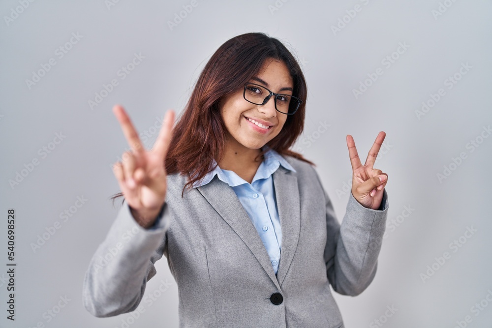 Hispanic young business woman wearing glasses smiling looking to the camera showing fingers doing victory sign. number two. Hispanic young business woman wearing glasses smiling looking to the camera showing fingers doing victory sign. number two.