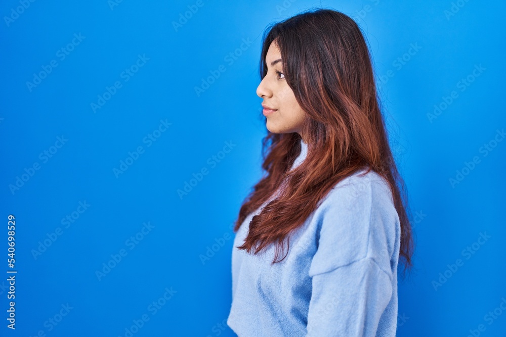 Hispanic young woman standing over blue background looking to side, relax profile pose with natural face and confident smile. Hispanic young woman standing over blue background looking to side, relax profile pose with natural face and confident smile.