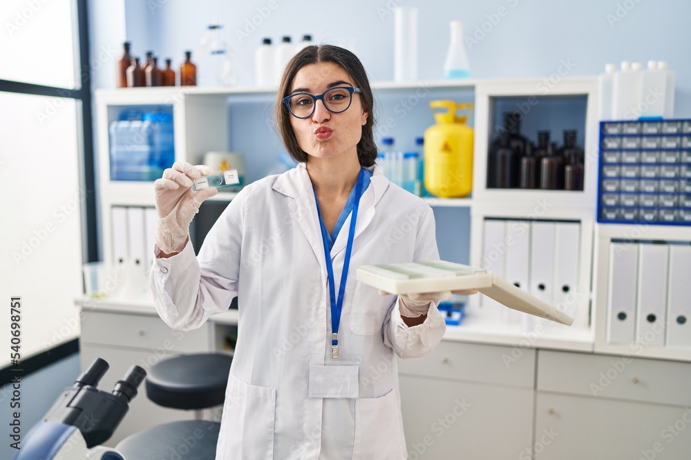 Young hispanic woman working at scientist laboratory with blood samples looking at the camera blowing a kiss being lovely and sexy. love expression. Young hispanic woman working at scientist laboratory with blood samples looking at the camera blowing a kiss being lovely and sexy. love expression.