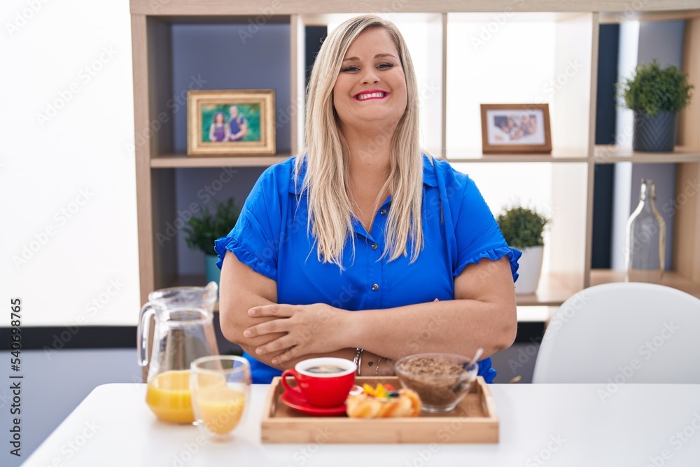 Caucasian plus size woman eating breakfast at home happy face smiling with crossed arms looking at the camera. positive person.