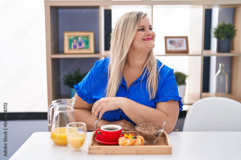Caucasian plus size woman eating breakfast at home looking away to side with smile on face, natural expression. laughing confident.