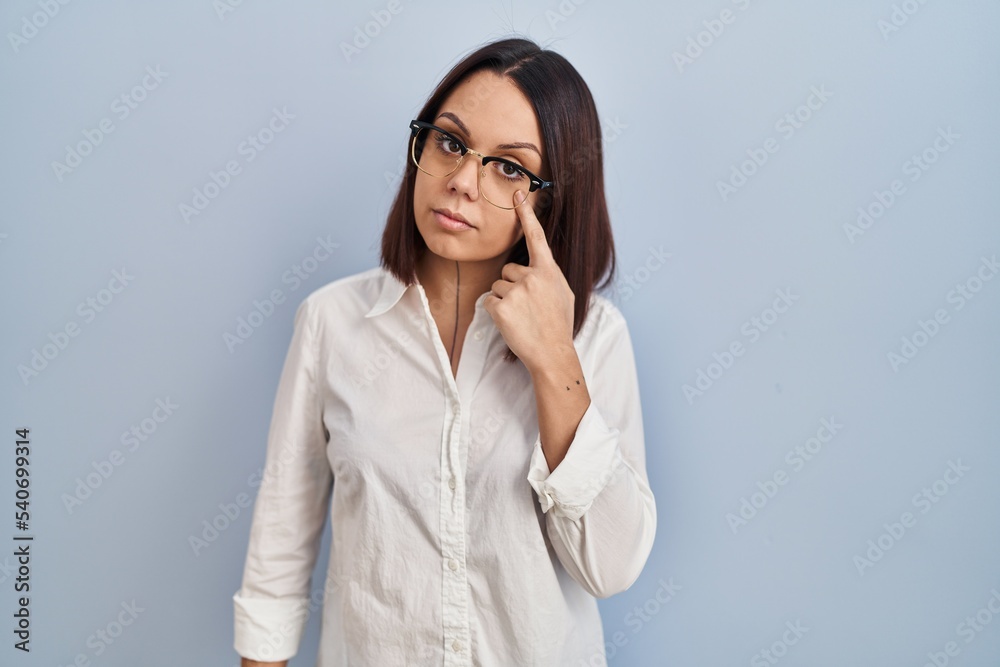 Young hispanic woman standing over white background pointing to the eye watching you gesture, suspicious expression Young hispanic woman standing over white background pointing to the eye watching you gesture, suspicious expression