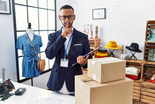 African american man working as manager at retail boutique asking to be quiet with finger on lips. silence and secret concept.