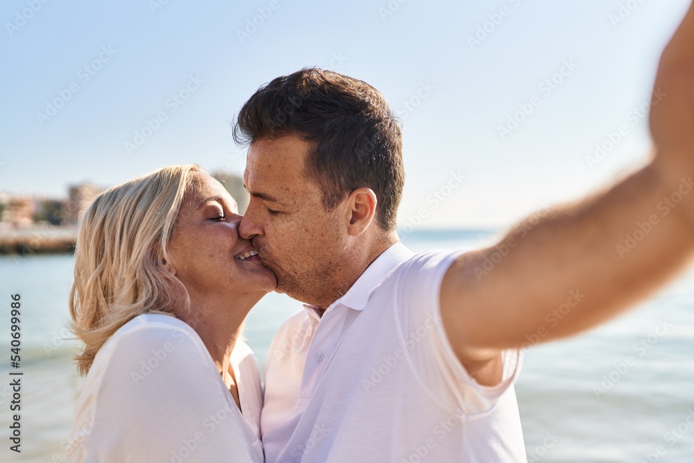 Middle age man and woman couple hugging each other and kissing make selfie by the smartphone at seaside Middle age man and woman couple hugging each other and kissing make selfie by the smartphone at seaside