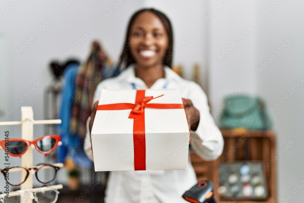 Young african american shopkeeper woman smiling happy holding gift at clothing store.