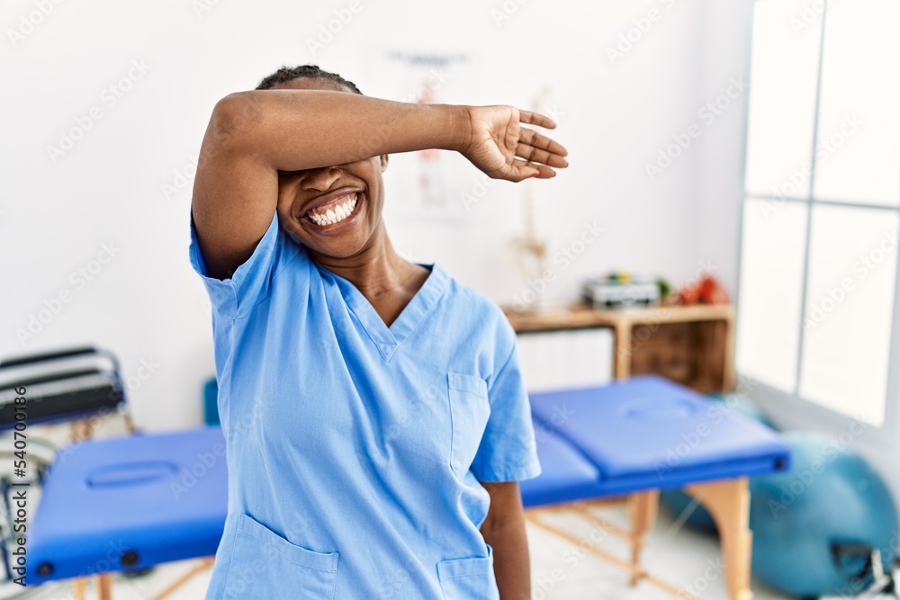 Obraz premium Black woman with braids working at pain recovery clinic covering eyes with arm smiling cheerful and funny. blind concept.
