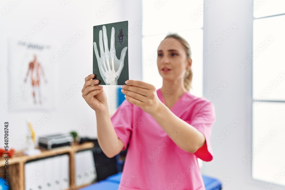 Young blonde woman wearing physiotherapist uniform looking xray at physiotherapy clinic Young blonde woman wearing physiotherapist uniform looking xray at physiotherapy clinic