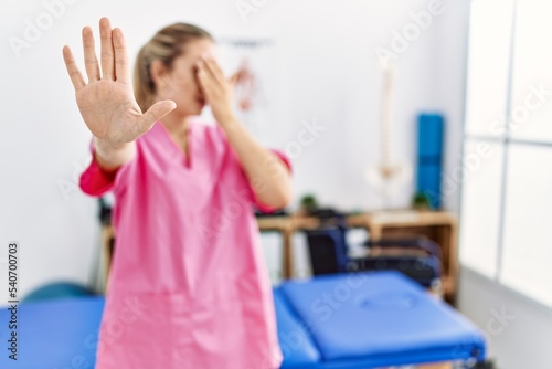 Young blonde woman working at pain recovery clinic covering eyes with hands and doing stop gesture with sad and fear expression. embarrassed and negative concept.